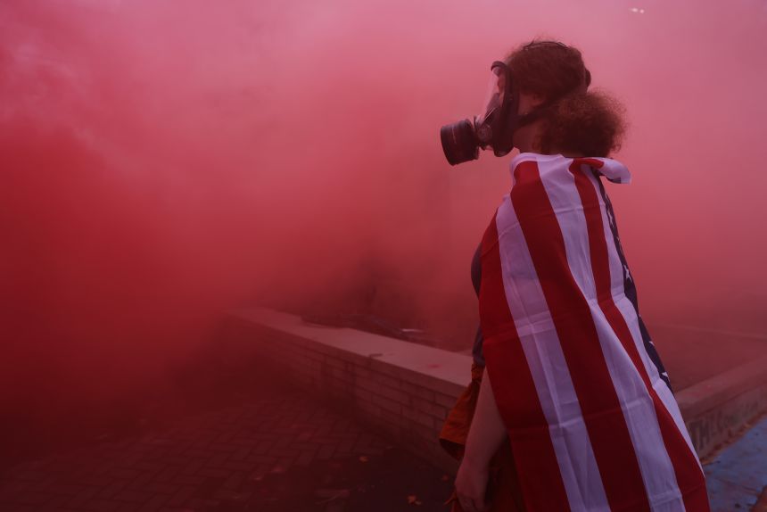 A protester stands in the haze from a smoke grenade outside of a downtown US Immigration and Customs Enforcement (ICE) facility in Portland, Oregon, Saturday.