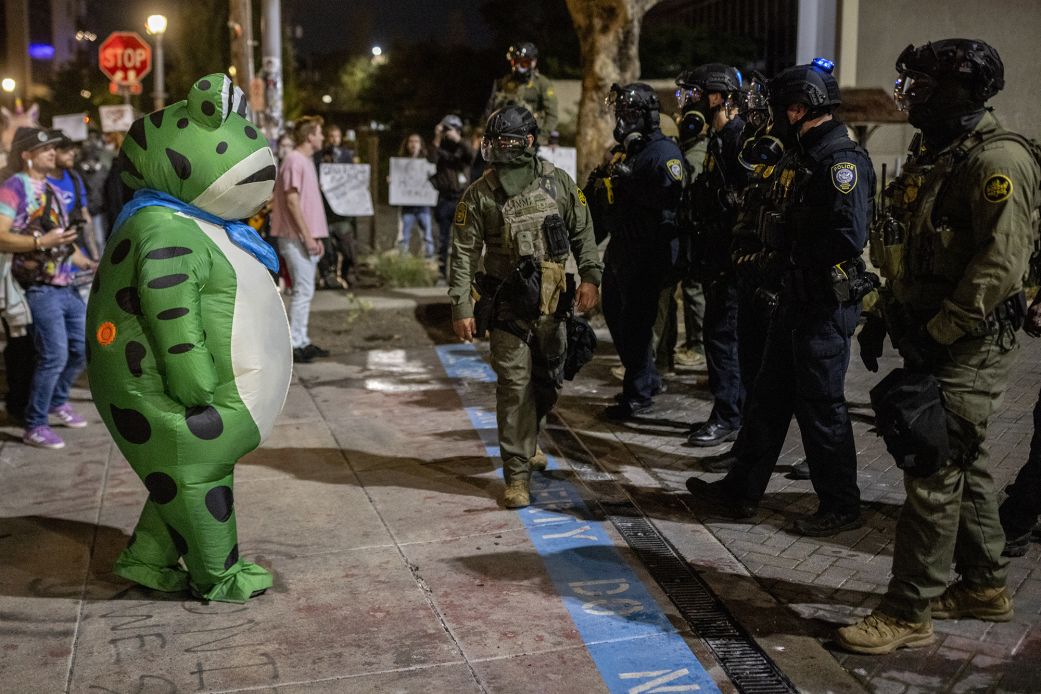 A protester in a frog costume stands in front of a line of federal law enforcement officers outside an ICE facility in Portland, Oregon.