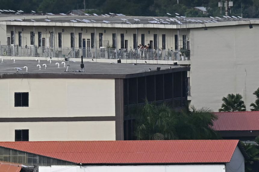 People on a balcony of a building with what appears to be Starlink satellite dishes on the roof in the KK Park complex in Myanmar's eastern Myawaddy township, as pictured from Mae Sot district in Thailand's border province of Tak, on September 17, 2025.