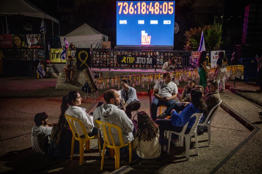 People sit and talk in front of a clock counting the days the hostages have been in captivity at Hostages Square in Tel Aviv, Israel on Monday.