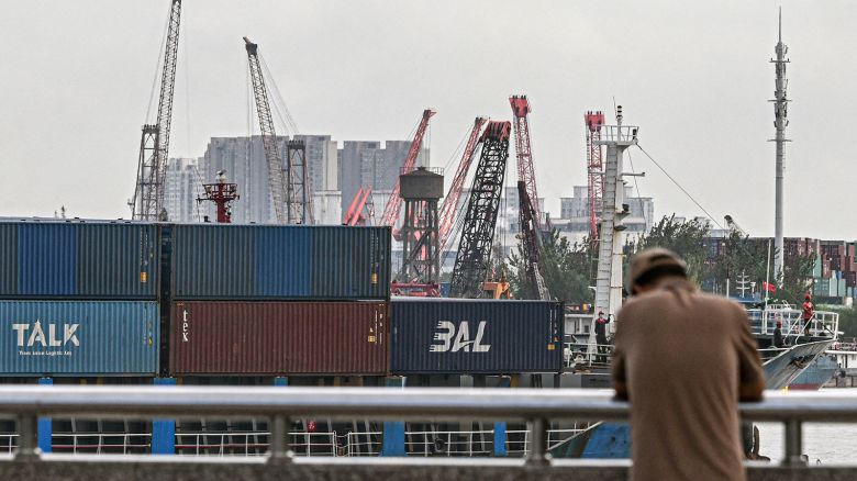 A man stands as a cargo ship carrying containers sails into a dock at a container terminal in Shanghai, on October 17, 2025.