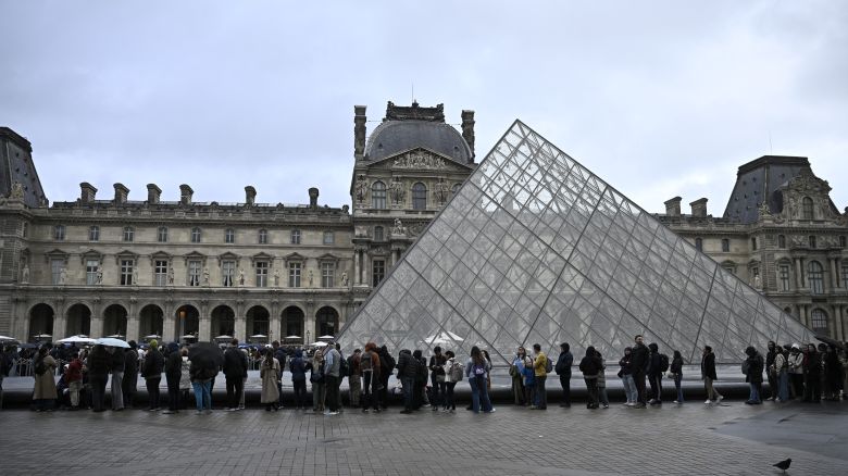 People queue in the Louvre pyramid courtyard moments before the announcement the museum will remain closed for a second day running after thieves stole crown jewels from the museum in Paris a day earlier, in Paris on October 20, 2025.