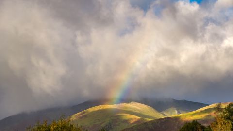 KESWICK, ENGLAND - OCTOBER 22: A rainbow appears between the autumn storm clouds over Blencathra on October 22, 2025 in Keswick, England. Autumn colours are expected to be more vibrant this year due to the warm and sunny summer, according to Forestry England. The warm and sunny conditions caused trees to produce more sugar in their leaves, which yields brighter colours.  (Photo by Christopher Furlong/Getty Images)