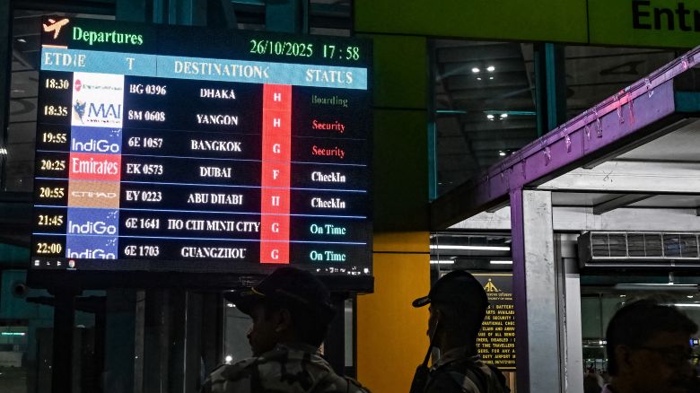 Security personnel stand near a flight information board at the Netaji Subhas Chandra Bose International Airport in Kolkata on October 26, 2025.