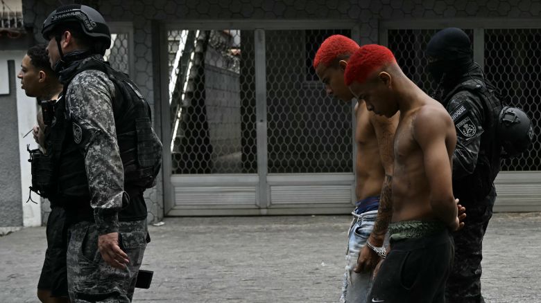 Police officers escort suspects arrested during the Operacao Contencao (Operation Containment) out of the Vila Cruzeiro favela, in the Penha complex, in Rio de Janeiro, Brazil, on October 28, 2025. At least 2,500 agents took part in an operation to arrest drug traffickers from the Comando Vermelho (CV), which resulted in, at least, 18 suspects and several police officers dead. (Photo by Mauro PIMENTEL / AFP) (Photo by MAURO PIMENTEL/AFP via Getty Images)          