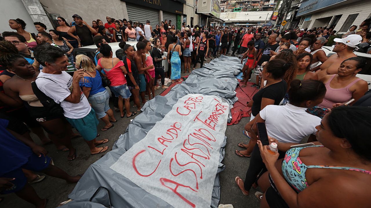 RIO DE JANEIRO, BRAZIL - OCTOBER 29: (EDITOR'S NOTE: Image depicts death.) People stand next to the bodies with a sign that reads "Claudio Castro (Rio de Janeiro governor) assassin and terrorist" in the Penha neighborhood a day after a massive anti-gang police operation took place at the Complexo da Penha and Alemao favelas on October 29, 2025 in Rio de Janeiro, Brazil. The 'Operação Contenção' is considered the biggest of its kind in Rio de Janeiro, with more than 120 people reported dead, including 4 police officers among those. The operation targeted the Comando Vermelho, one of the biggest criminal gangs in the city.  (Photo by Wagner Meier/Getty Images)