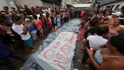 RIO DE JANEIRO, BRAZIL - OCTOBER 29: (EDITOR'S NOTE: Image depicts death.) People stand next to the bodies with a sign that reads "Claudio Castro (Rio de Janeiro governor) assassin and terrorist" in the Penha neighborhood a day after a massive anti-gang police operation took place at the Complexo da Penha and Alemao favelas on October 29, 2025 in Rio de Janeiro, Brazil. The 'Operação Contenção' is considered the biggest of its kind in Rio de Janeiro, with more than 120 people reported dead, including 4 police officers among those. The operation targeted the Comando Vermelho, one of the biggest criminal gangs in the city.  (Photo by Wagner Meier/Getty Images)