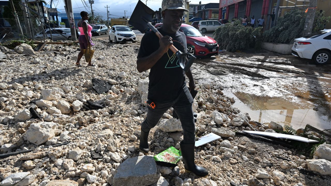 A man walks with a shovel in hand over rubble on Main Street in Santa Cruz, St. Elizabeth, Jamaica on October 29, 2025. Hurricane Melissa ripped up trees and knocked out power after making landfall in Jamaica on October 28, 2025 as one of the most powerful hurricanes on record, inundating the island nation with rains that threaten flash floods and landslides. (Photo by Ricardo MAKYN / AFP) (Photo by RICARDO MAKYN/AFP via Getty Images)          