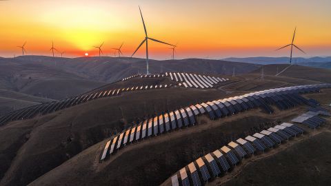 In an aerial view, sunset glow lights up wind turbines and rows of solar panels at a wind farm on October 28, 2025 in Qingyang, Gansu Province of China.