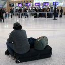 A traveler sits on his luggage as he waits at Newark Liberty International Airport Newark, New Jersey, on November 7, 2025. Hundreds of flights were canceled across the United States on Friday after the Trump administration ordered reductions to ease strain on air traffic controllers who are working without pay amid congressional paralysis on funding the US budget.