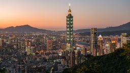 Night view of Taipei 101 and the Taipei skyline in the distance behind vegetation and a mountain trail from Taipei Mountains in Taipei,  Taiwan, on December 14, 2021.
