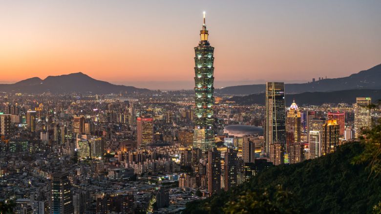 Night view of Taipei 101 and the Taipei skyline in the distance behind vegetation and a mountain trail from Taipei Mountains in Taipei,  Taiwan, on December 14, 2021.