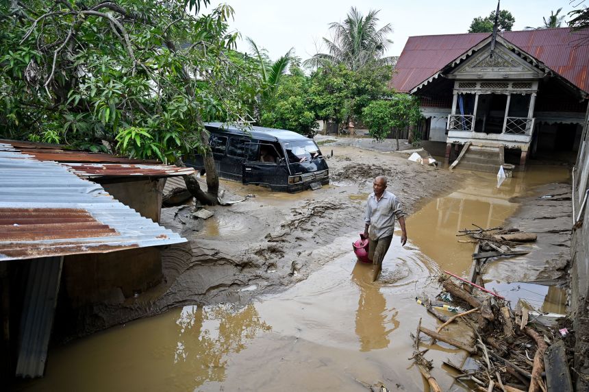 A man wades through the floodwaters following flash floods in Meureudu, in Indonesia's Aceh province, on November 28. (Photo by Chaideer MAHYUDDIN / AFP via Getty Images)