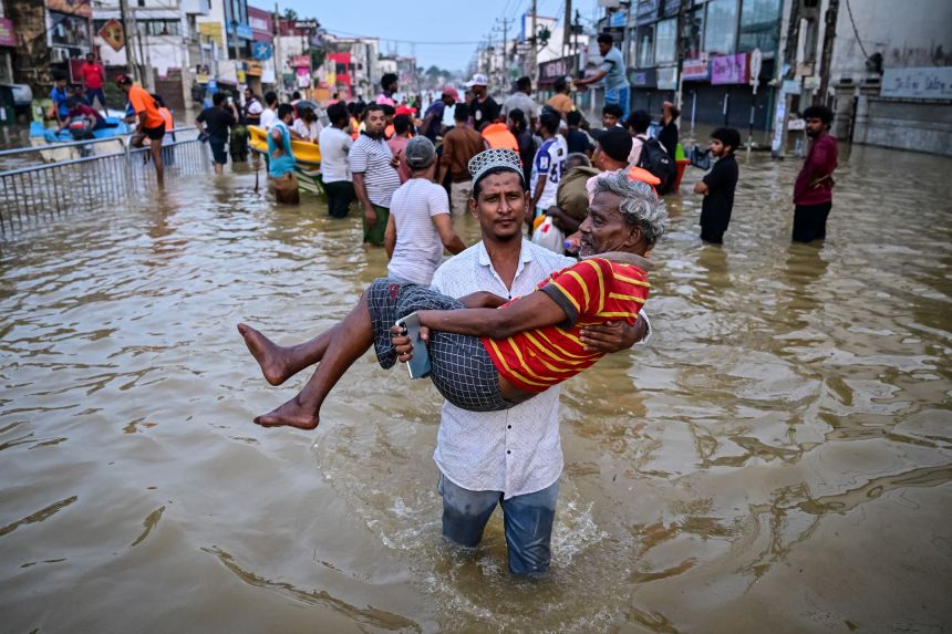 A man is carried through a flooded road after heavy rains in the Colombo suburb of Wellampitiya on November 30, 2025.