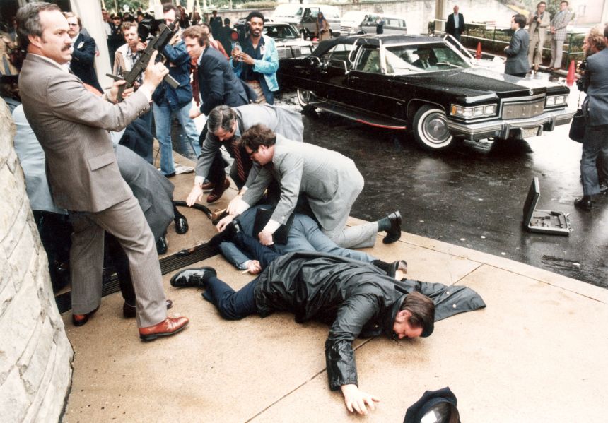 Men, including one with an automatic rifle, scramble after the March 30, 1981, assassination attempt on President Ronald Reagan in Washington, DC.