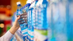 Female hand taking bottle of mineral water from supermarket shelf