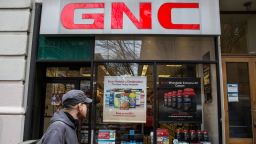 A man walks past a GNC store with supplement posters in its windows. 