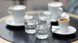 Three cups of fresh coffee (espresso and latte) and three glass with still water on table of Parisian outdoors cafe