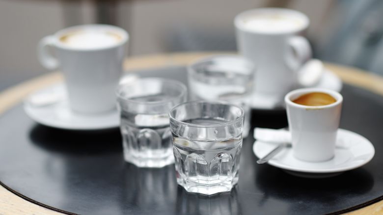 Three cups of fresh coffee (espresso and latte) and three glass with still water on table of Parisian outdoors cafe