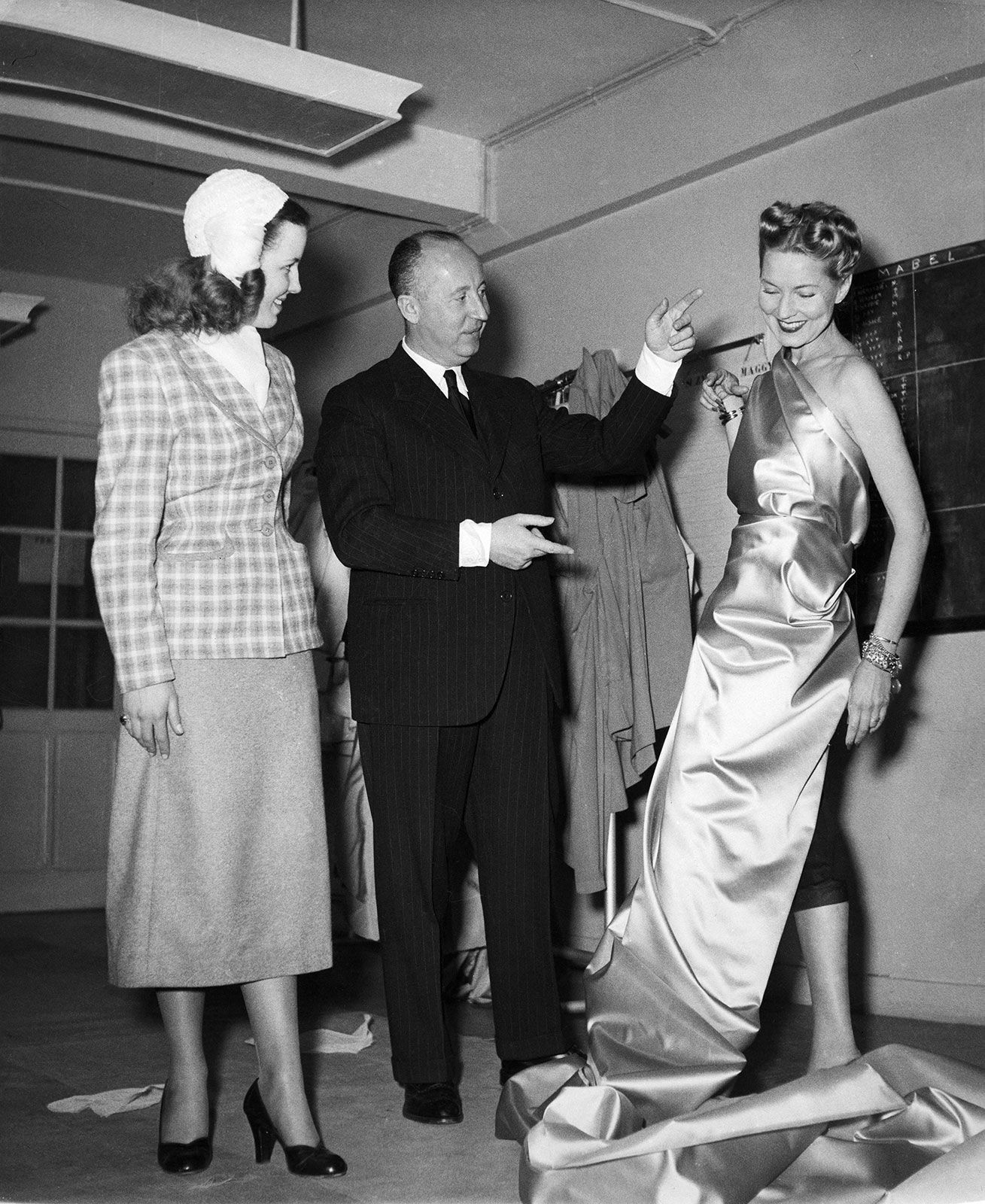 Dior is pictured here in his fashion studio, making adjustments on a fit model.