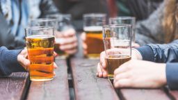 Hands holding glasses with beer on a table at pub in London. A group of friends is enjoying beer time in the city, close up on the glasses.