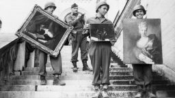 (Original Caption) 5/22/45-Fussen, Germany: While a lieutenant checks his list in the background, 7th army soldiers carry three valuable paintings down the steps of Neuschwanstein Castle at Fussen, Germany, where they were a part of the collection looted by the Nazis from conquered countries. The paintings are, (L to R) "Cat and Mirror," Charbin, 1749; a painting by Brouver, belonging to the Weissman Collection; and a portrait of a lady marked "Rothschild Collection 18th Century."
