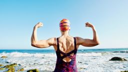 Older Caucasian woman flexing her muscles on beach