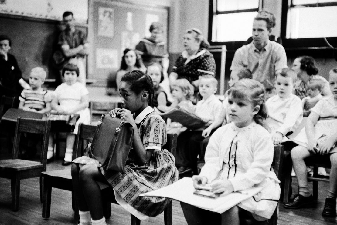 Six-year-old Lasuanda Faye Griffith, foreground left, peers warily from behind her school bag as she sits in a first-grade classroom at Glenn Elementary School in Nashville, Tennessee, on September 9, 1957 — the first day after the school was integrated. Sitting with her are other students and a number of adults, apparently the parents of some of the children.