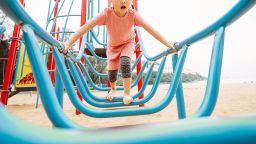 Lovely little girl playing joyfully with the climbing equipments in sand playground.