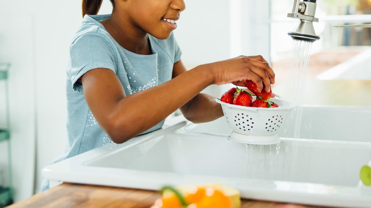 Black girl washing strawberries in kitchen
