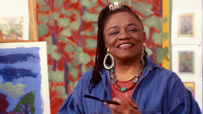 Portrait of American artist Faith Ringgold as she poses in front of one of her paintings in her studio, New York, New York, 1999.
