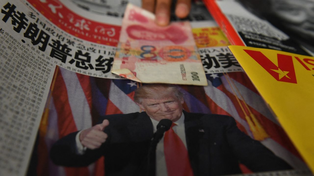 TOPSHOT - A vendor picks up a 100 yuan note above a newspaper featuring a photo of US president-elect Donald Trump, at a news stand in Beijing on November 10, 2016. The world's second-largest economy is US president-elect Donald Trump's designated bogeyman, threatening it on the campaign trail with tariffs for stealing American jobs, but analysts say US protectionism could create opportunities for Beijing. (Photo by GREG BAKER / AFP) (Photo by GREG BAKER/AFP via Getty Images)
