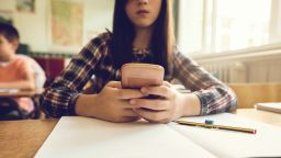 Close up of elementary student typing text message on smart phone while sitting at the desk in the classroom.