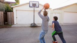 Caucasian brothers playing basketball near garage