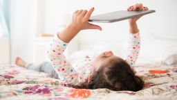 Mixed Race girl laying on bed using digital tablet