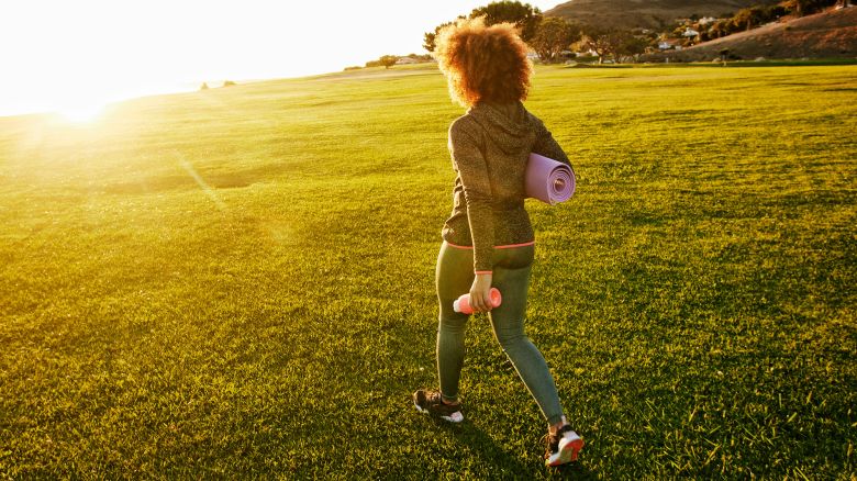 Hispanic woman carrying exercise mat in sunny field
