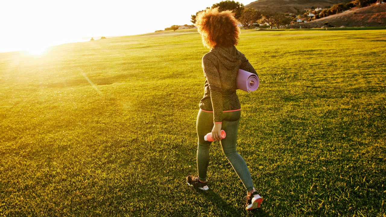 Hispanic woman carrying exercise mat in sunny field