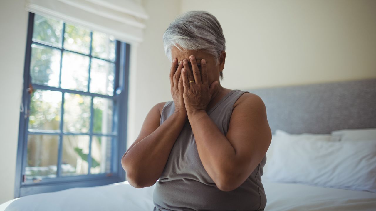 Upset senior woman covering her face at home