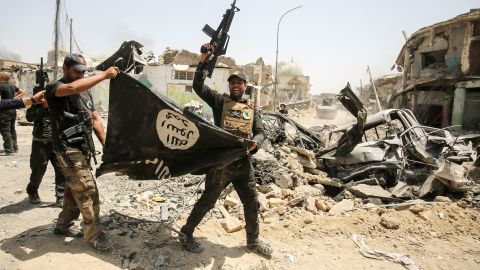  of the Iraqi Counter-Terrorism Service (CTS) cheer as they carry upside-down a black flag of the Islamic State (IS) group, with the destroyed Al-Nuri mosque seen in the background, in the Old City of Mosul on July 2, 2017, during the offensive to retake the city from IS fighters. Explosions on the evening of June 21, 2017 levelled the mosque where Abu Bakr al-Baghdadi gave his first sermon as leader of the Islamic State group, along with its ancient minaret. (Photo by AHMAD AL-RUBAYE / AFP) (Photo by AHMAD AL-RUBAYE/AFP via Getty Images)
