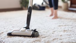 Young woman using a vacuum cleaner while cleaning carpet in the house.