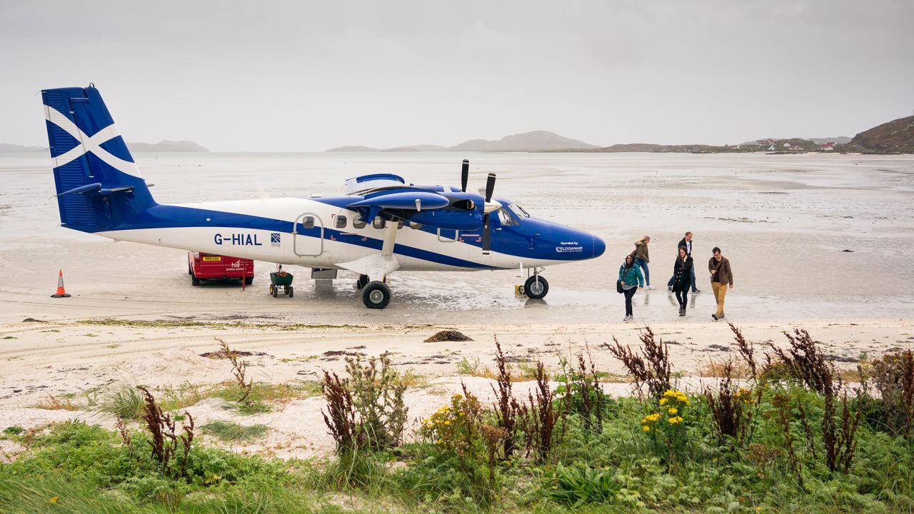 Isle of Barra, Scotland, UK - Recently arrived passengers walking on the beach from the Loganair operated Twin Otter plane, having landed at Barra Airport. At low tide, the beach is used as the airport's runway on the Outer Hebridean island.