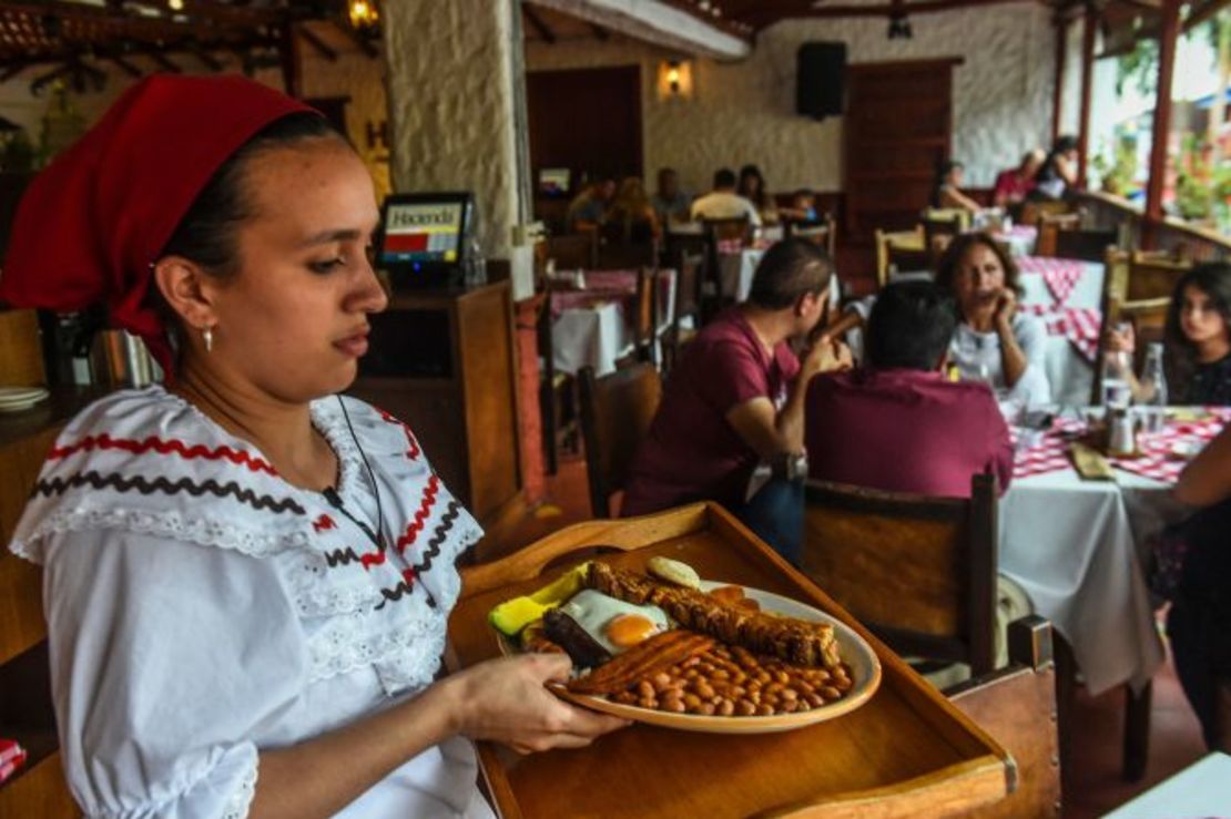 Medellín, Colombia: una mesera lleva un plato de bandeja paisa, un plato de la región de Antioquia, compuesto de frijoles, arroz, chorizo, morcilla, carne picada, piel de cerdo frita, plátano, huevo frito y aguacate.