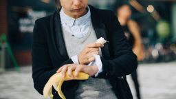 Woman checking time while eating banana at city