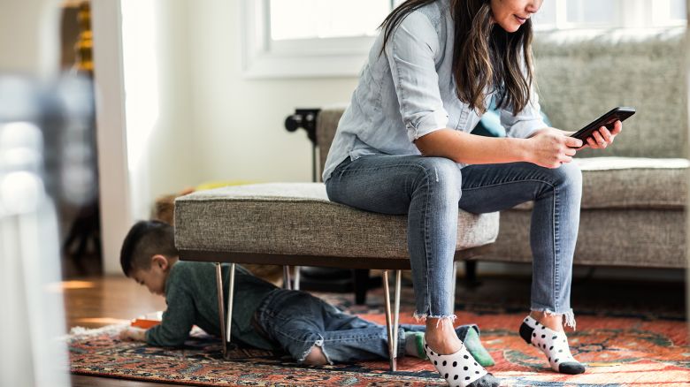 Woman using smartphone at home with child in background