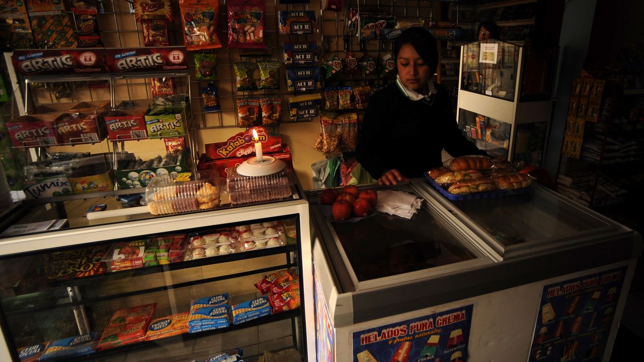 A clerk works at a grocery by candlelight the night of November 12, 2009 in Quito during a blackout as part of the government's plan to save energy.  AFP PHOTO / RODRIGO BUENDIA (Photo credit should read RODRIGO BUENDIA/AFP via Getty Images)