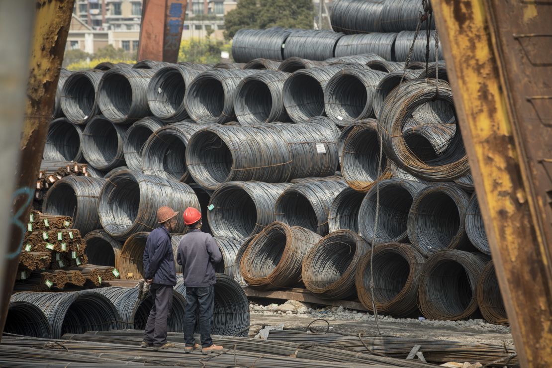 Workers stand in front of coils of steel wire at a depot on the outskirts of Shanghai on March 26, 2018.