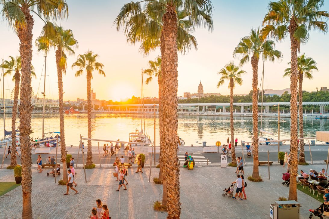 People walk on the Paseo del Mullene Uno waterfront promenade in downtown Malaga Spain at sunset time.