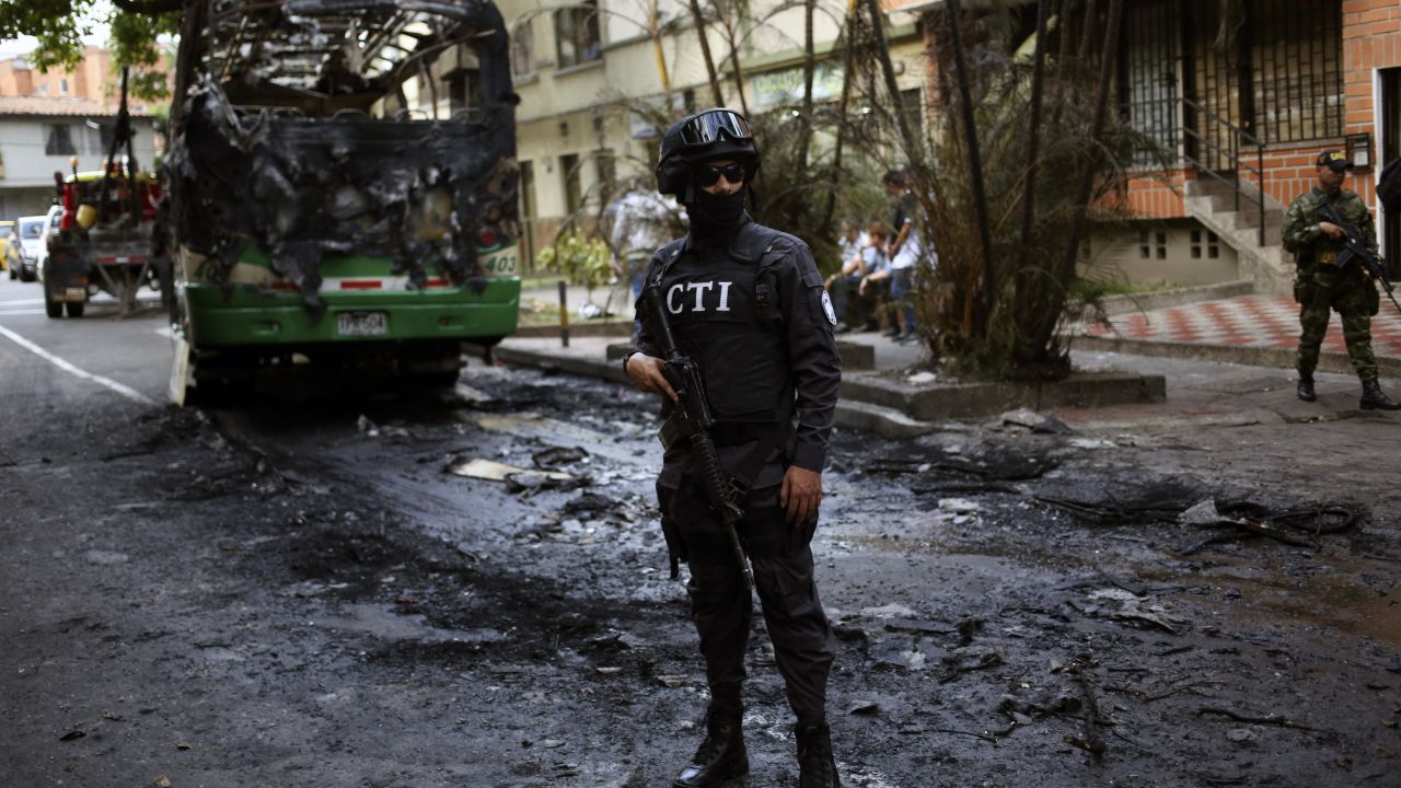 TOPSHOT - A member of the Technical Investigation Team (CTI) stands guard next to a bus burnt by criminal gang  near Comuna 13 neighborhood, Medellin, Antioquia department, Colombia on April 26, 2018. The Comuna 13 Neighborhood has been militarized following an increase in gang violence over the last days due to the capture of several leaders including Cristian Camilo Mazo Castaneda, aka ÒSombra, leader of the Robledo Gang. (Photo by JOAQUIN SARMIENTO / AFP) (Photo by JOAQUIN SARMIENTO/AFP via Getty Images)          