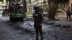 TOPSHOT - A member of the Technical Investigation Team (CTI) stands guard next to a bus burnt by criminal gang members near Comuna 13 neighborhood, Medellin, Antioquia department, Colombia on April 26, 2018. The Comuna 13 Neighborhood has been militarized following an increase in gang violence over the last days due to the capture of several leaders including Cristian Camilo Mazo Castaneda, aka ÒSombra, leader of the Robledo Gang. (Photo by JOAQUIN SARMIENTO / AFP) (Photo by JOAQUIN SARMIENTO/AFP via Getty Images)