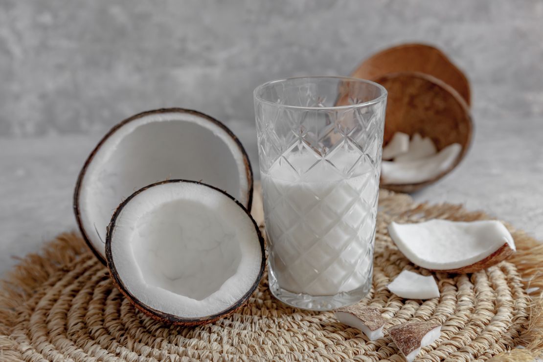 glass-of-homemade-coconut-milk-with-opened-coconuts-on-rattan-placemat.jpg